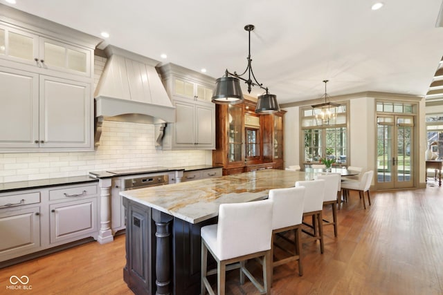 kitchen with custom range hood, light wood-type flooring, backsplash, and a center island