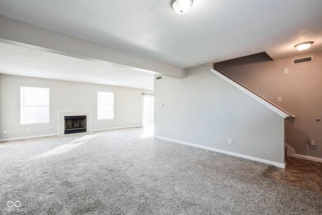 unfurnished living room with a tile fireplace, a textured ceiling, and carpet