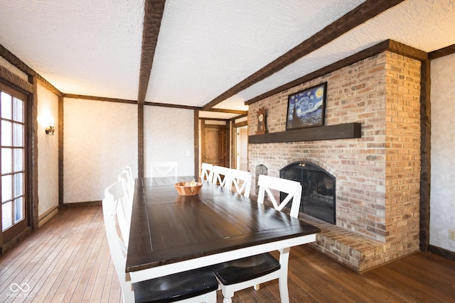 dining room with hardwood / wood-style flooring, a fireplace, a textured ceiling, and beamed ceiling