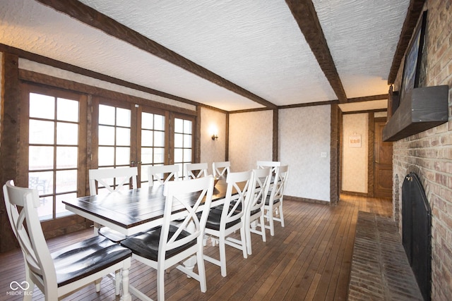 dining space with a textured ceiling, dark hardwood / wood-style flooring, a brick fireplace, french doors, and beamed ceiling