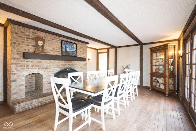 dining space with beamed ceiling, a brick fireplace, hardwood / wood-style floors, and a textured ceiling