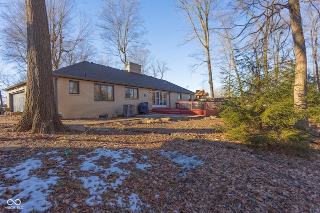 snow covered back of property with a garage, a wooden deck, and central air condition unit