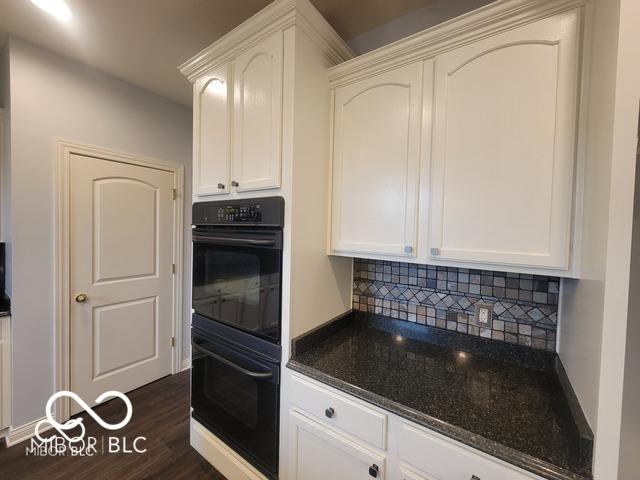 kitchen featuring double oven, tasteful backsplash, white cabinetry, dark hardwood / wood-style flooring, and dark stone counters