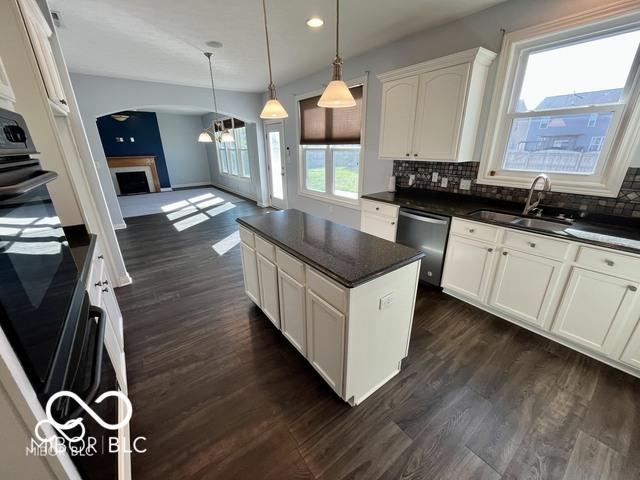 kitchen with hanging light fixtures, white cabinets, a kitchen island, decorative backsplash, and stainless steel dishwasher