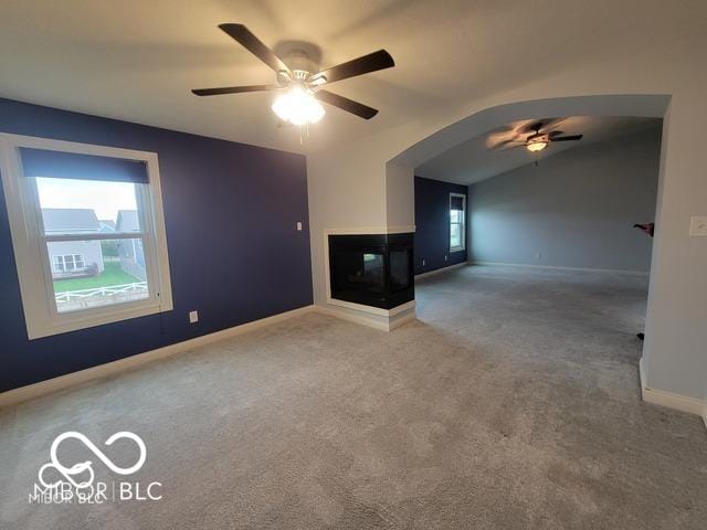 unfurnished living room with carpet flooring, lofted ceiling, ceiling fan, and a multi sided fireplace