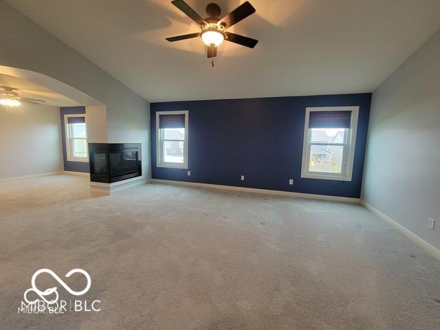 unfurnished living room featuring ceiling fan, a multi sided fireplace, lofted ceiling, and light colored carpet