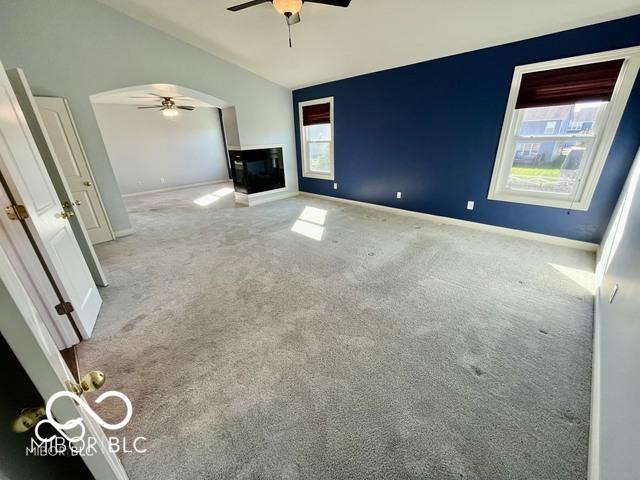 unfurnished living room with vaulted ceiling, a healthy amount of sunlight, light colored carpet, and ceiling fan