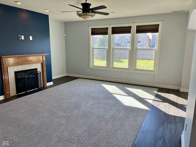 unfurnished living room with ceiling fan, dark hardwood / wood-style floors, a tile fireplace, and a wealth of natural light