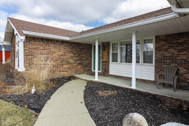 view of exterior entry featuring brick siding and roof with shingles