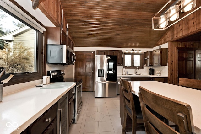 kitchen featuring vaulted ceiling, light tile patterned flooring, appliances with stainless steel finishes, dark brown cabinets, and wooden ceiling