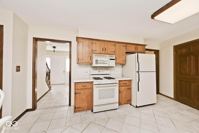 kitchen featuring white appliances, brown cabinetry, baseboards, light countertops, and backsplash