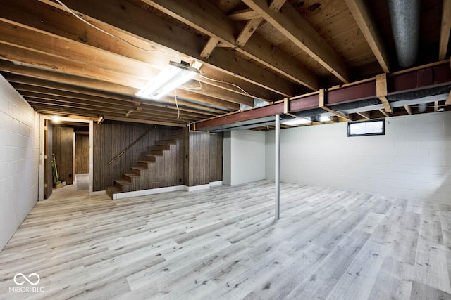 basement with stairway, concrete block wall, and wood finished floors