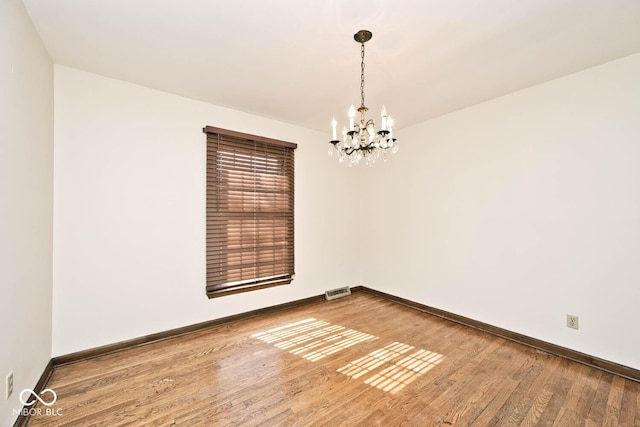 spare room with visible vents, an inviting chandelier, baseboards, and hardwood / wood-style floors