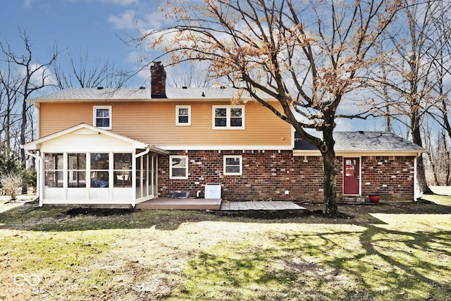 rear view of house with brick siding, a lawn, a chimney, and a sunroom