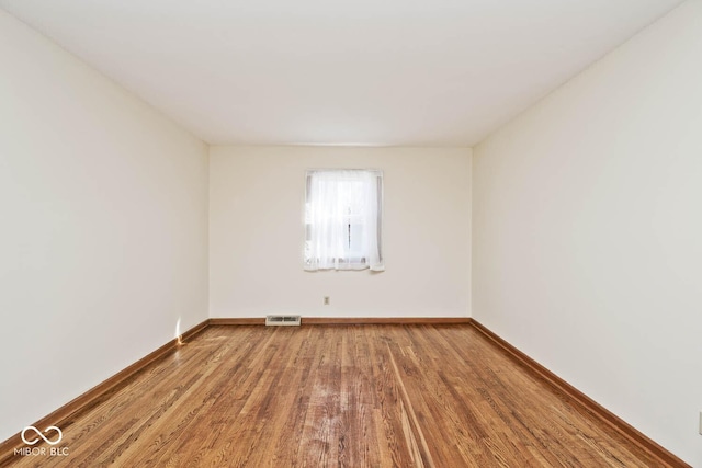 spare room featuring wood finished floors, visible vents, and baseboards