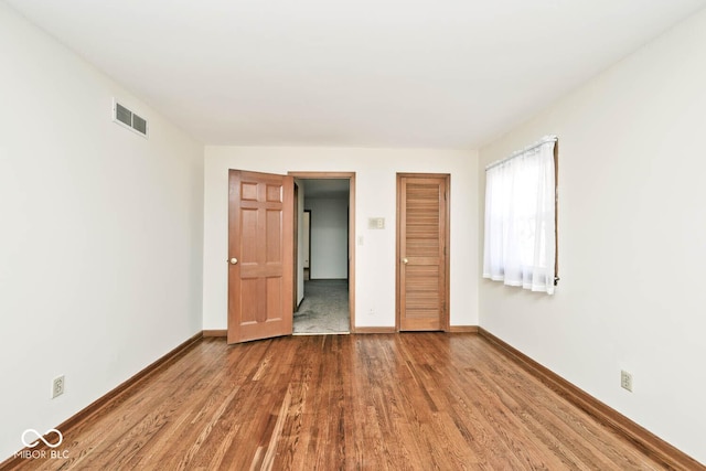 unfurnished bedroom with a closet, visible vents, baseboards, and wood finished floors