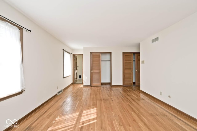 unfurnished bedroom featuring visible vents, multiple closets, baseboards, and light wood finished floors