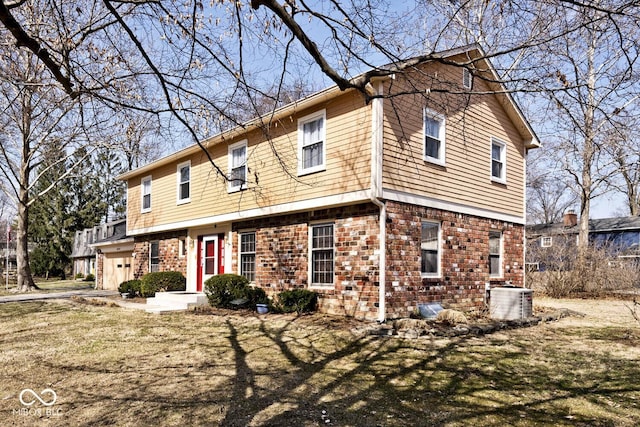 colonial home with a garage, central AC unit, and brick siding