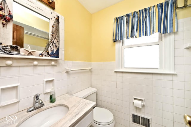 bathroom with visible vents, tile walls, toilet, wainscoting, and vanity