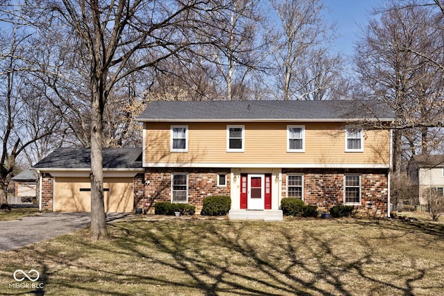 colonial inspired home with aphalt driveway, a front lawn, brick siding, and an attached garage