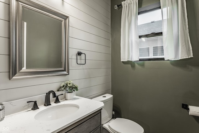 bathroom with vanity, toilet, and wood walls