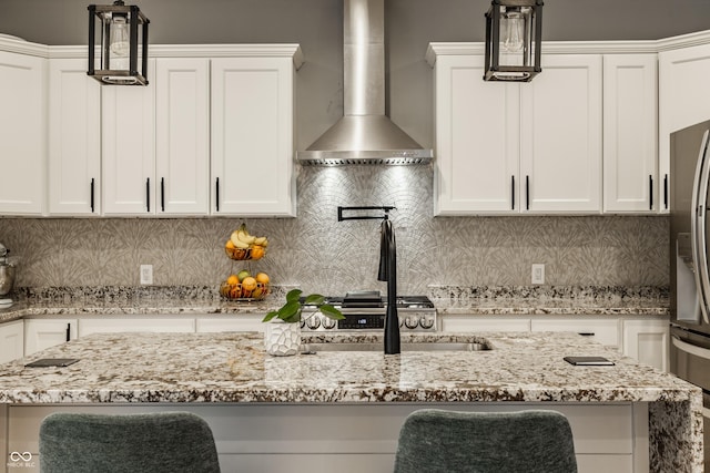 kitchen featuring tasteful backsplash, white cabinets, hanging light fixtures, light stone counters, and wall chimney exhaust hood