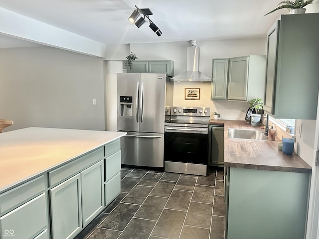 kitchen featuring butcher block countertops, wall chimney range hood, sink, dark tile patterned floors, and stainless steel appliances