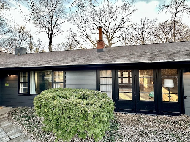 property entrance with french doors, a chimney, and a shingled roof