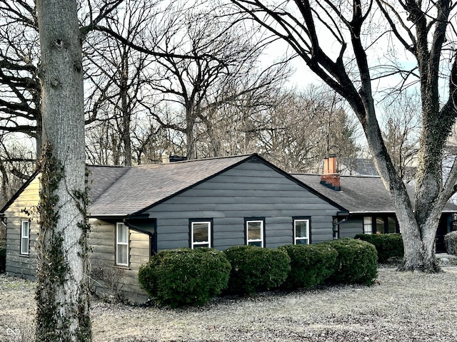 view of side of home with roof with shingles and a chimney