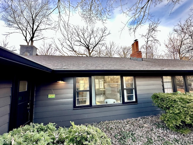 view of side of home with a chimney and roof with shingles