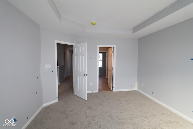 unfurnished bedroom with light carpet, a tray ceiling, and baseboards