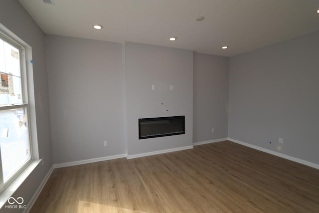 unfurnished living room with baseboards, wood finished floors, a glass covered fireplace, and recessed lighting