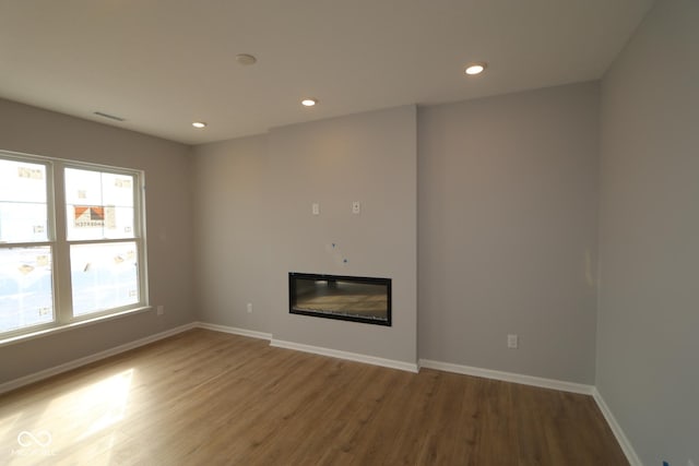 unfurnished living room with a glass covered fireplace, baseboards, and wood finished floors