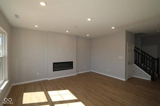 unfurnished living room featuring a glass covered fireplace, wood finished floors, recessed lighting, stairway, and baseboards