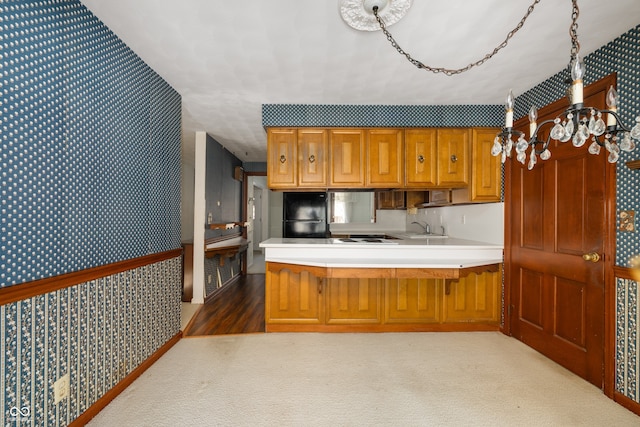 kitchen with sink, dark colored carpet, a notable chandelier, kitchen peninsula, and black fridge