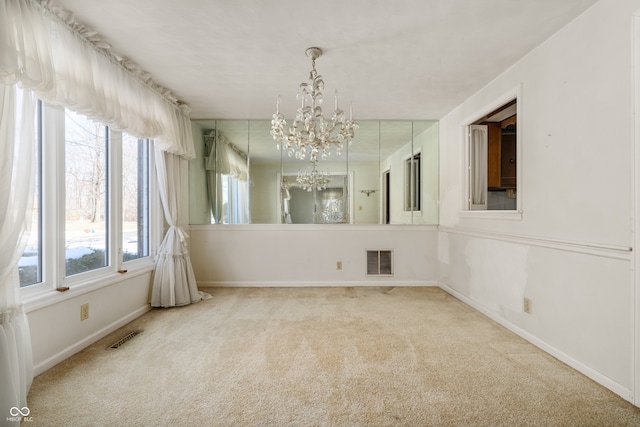 carpeted empty room with an inviting chandelier