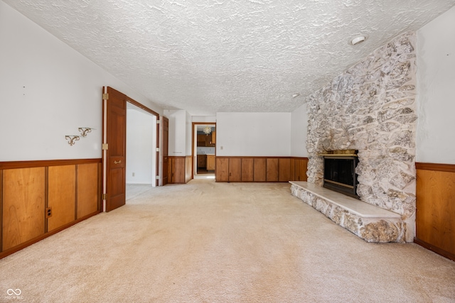 unfurnished living room featuring light colored carpet, a textured ceiling, a fireplace, and wood walls