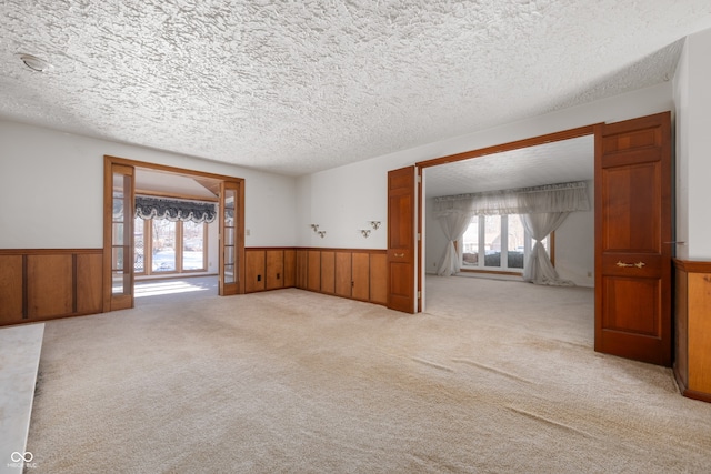 unfurnished room with light colored carpet, a textured ceiling, and wood walls