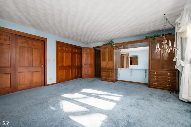 unfurnished bedroom featuring a notable chandelier, two closets, light colored carpet, and a textured ceiling