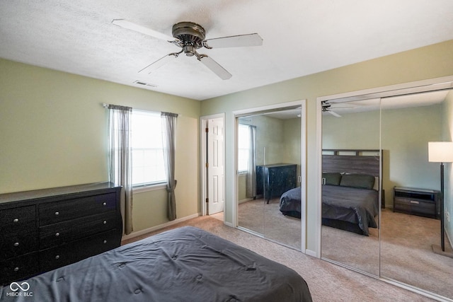 bedroom featuring ceiling fan, light colored carpet, and two closets