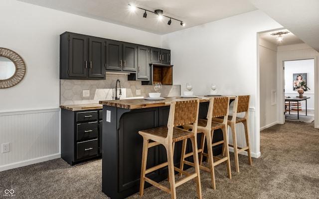 kitchen featuring dark carpet, tasteful backsplash, butcher block countertops, and a breakfast bar area