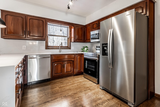 kitchen featuring tasteful backsplash, sink, stainless steel appliances, track lighting, and light hardwood / wood-style flooring