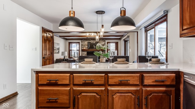 kitchen featuring wood-type flooring, decorative light fixtures, a brick fireplace, dishwasher, and kitchen peninsula