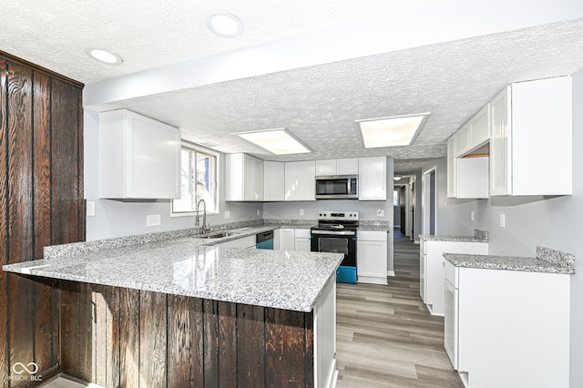 kitchen featuring sink, light hardwood / wood-style flooring, appliances with stainless steel finishes, white cabinets, and kitchen peninsula