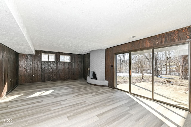 unfurnished living room featuring a fireplace, a textured ceiling, light hardwood / wood-style flooring, and wood walls