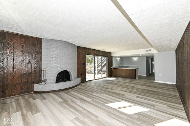 unfurnished living room featuring light hardwood / wood-style flooring, a textured ceiling, a fireplace, and wood walls