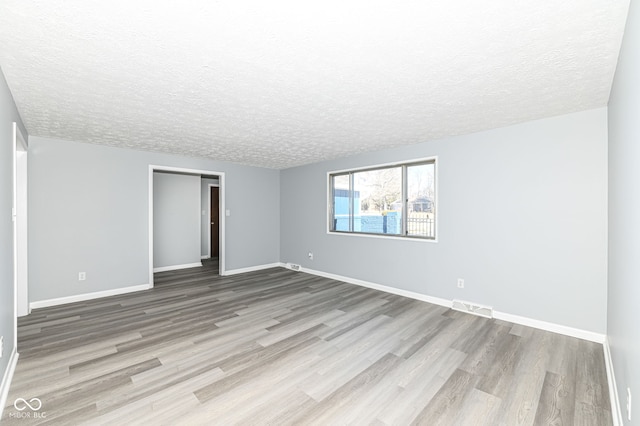 empty room with a textured ceiling and light hardwood / wood-style flooring