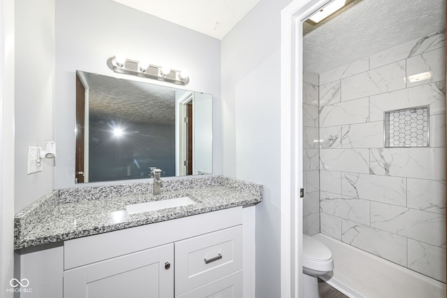 bathroom featuring vanity, tiled shower, a textured ceiling, and toilet