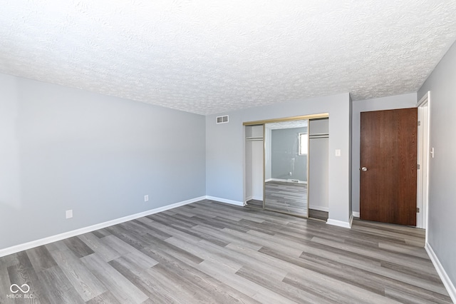 unfurnished bedroom with a textured ceiling, light wood-type flooring, and a closet