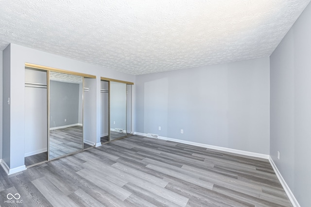 unfurnished bedroom with two closets, wood-type flooring, and a textured ceiling